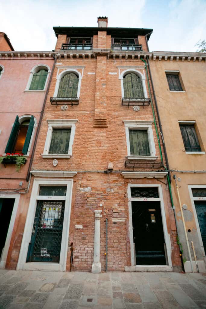A tall, narrow brick building with three floors, arched windows, and two doors at street level, this local gem sits between similar buildings and evokes the charm of old Venice.