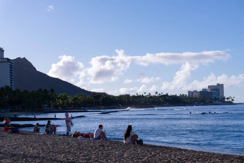 A group of people sitting on a beach in Waikiki, Hawaii, one of the top things to do in Oahu for couples.
