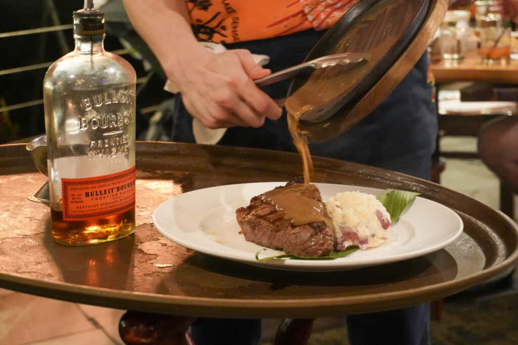 A server pouring a sauce on a plate while a couple enjoys one of the things to do in Oahu.