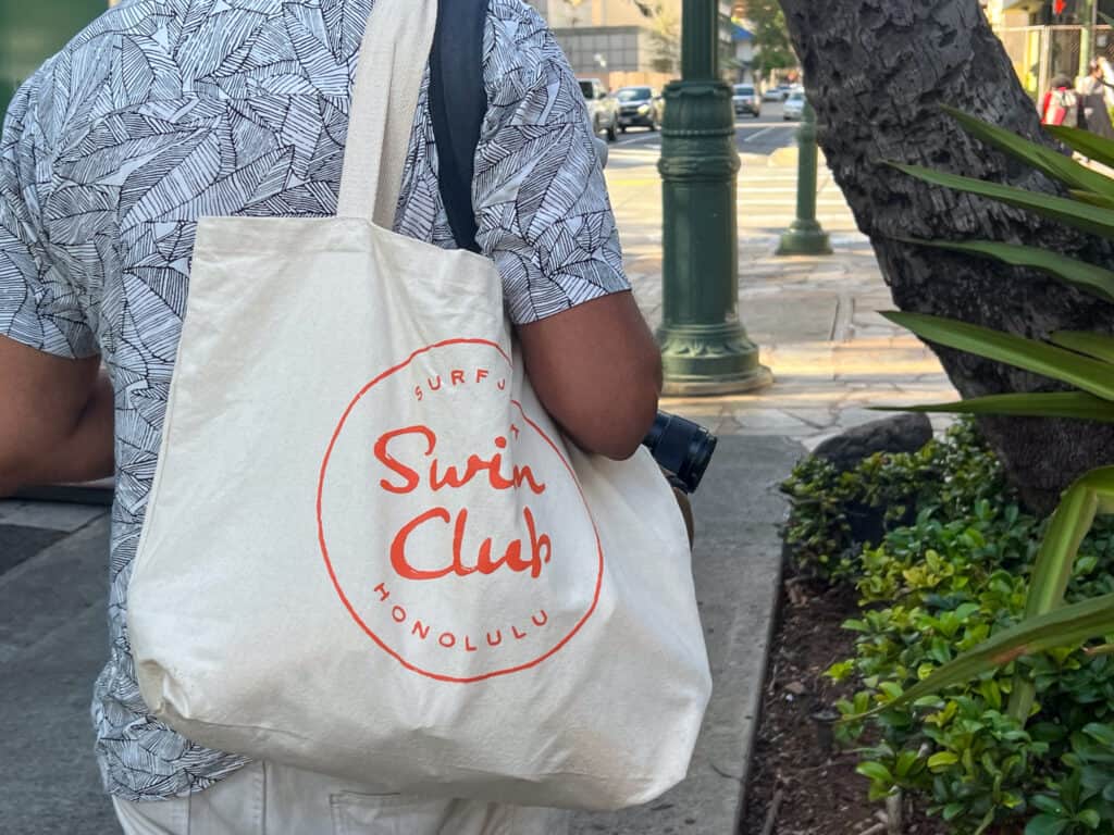 A man carrying a tote bag with the word swim club on it, representing one of the exciting things to do in Oahu for couples.