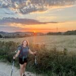 A woman named Jen with hiking poles standing on the Camino de Santiago road at sunrise.