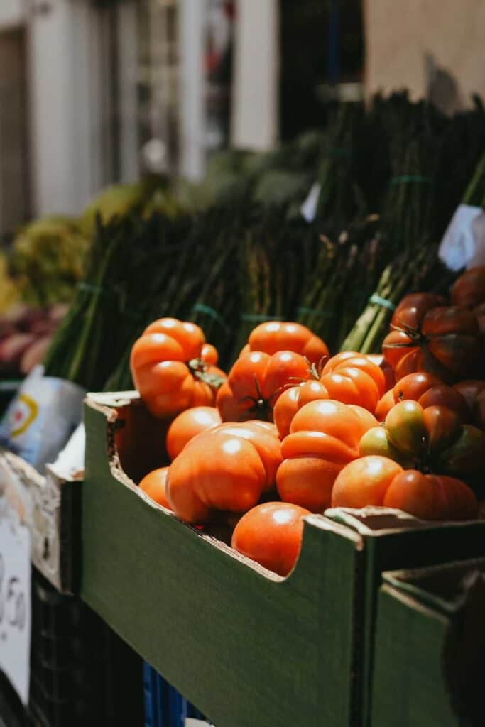 Crates of fresh tomatoes and asparagus arranged in a market stall under natural light.