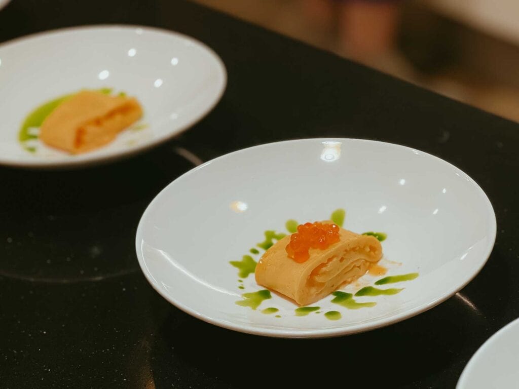 Slices of omelette topped with red caviar and garnished with green sauce are plated on white dishes.