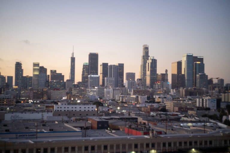 A wide-angle view of a city skyline with numerous high-rise buildings at dusk, perfect for planning your one day in Los Angeles itinerary. The foreground features an industrial area with warehouses and various structures, capturing the vibrant contrast of urban life.