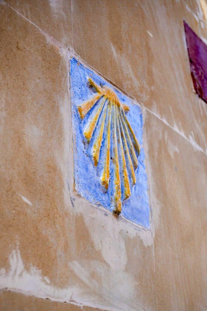 A blue ceramic tile with a yellow scallop shell design is embedded in a light-colored stucco wall.