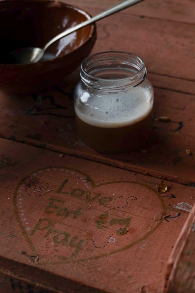 A glass jar of coffee and a bowl with a spoon sit on a wooden table featuring a heart outline with the text "Love Eat & Pray," perfect for the digital nomad seeking inspiration.