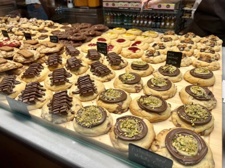 A display of assorted cookies, including chocolate, nut-topped, and fruit-filled varieties, on a wooden counter with small price signs, showcasing some of the best desserts in Barcelona.