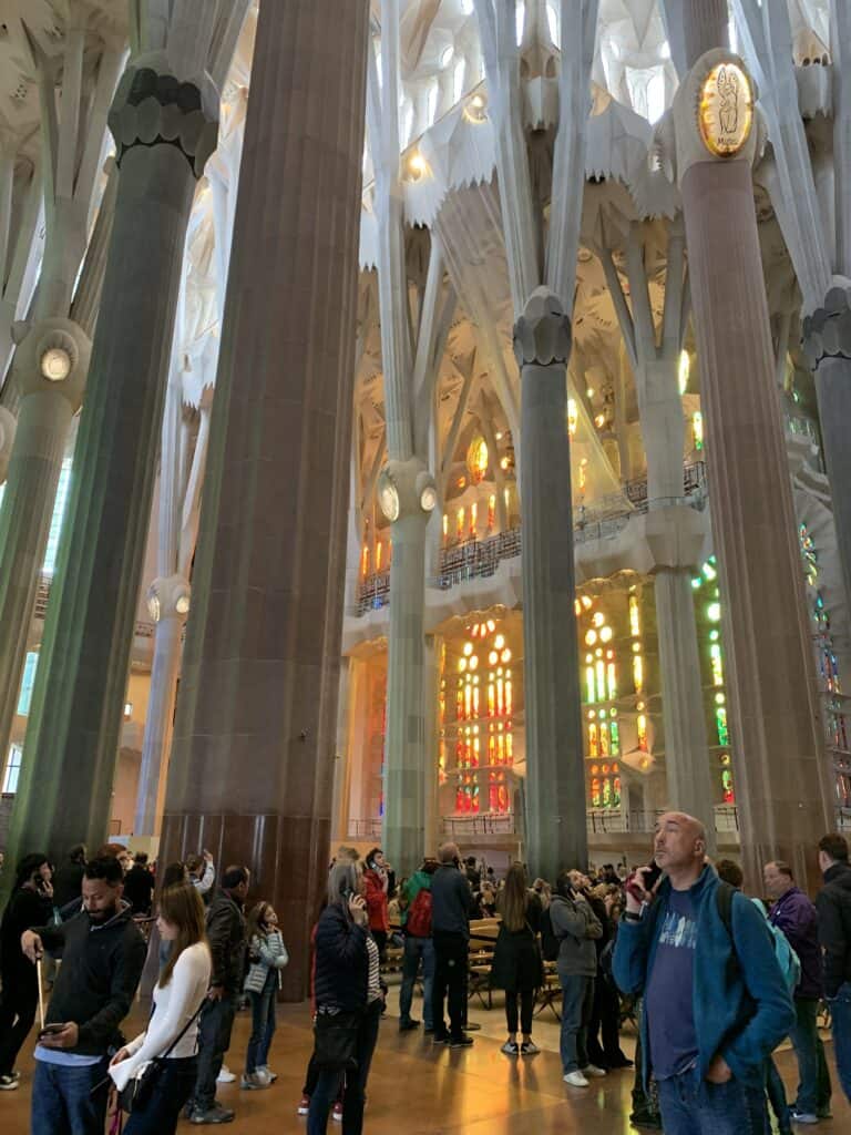 People standing inside a large cathedral with tall columns and colorful stained glass windows, awash in the warm glow that only Barcelona in the summer can provide.