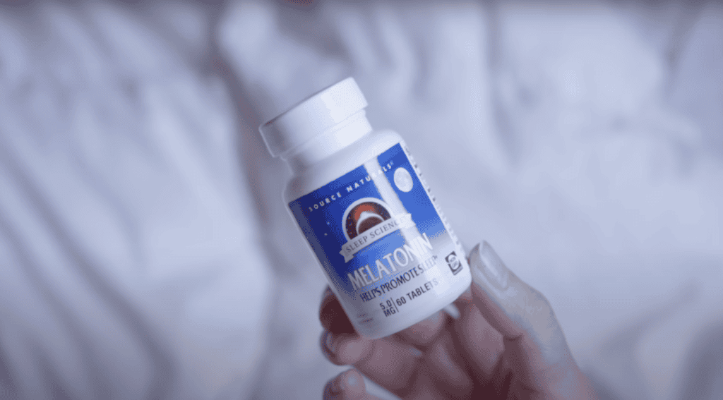A hand holds a bottle of melatonin tablets, perfect for anyone sleeping on the Camino, with a blue label featuring a crescent moon and stars.