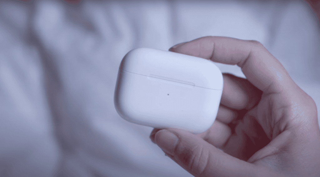 A hand holding a white wireless earbuds case against a blurred background, reminiscent of the tranquility felt when sleeping on the Camino.
