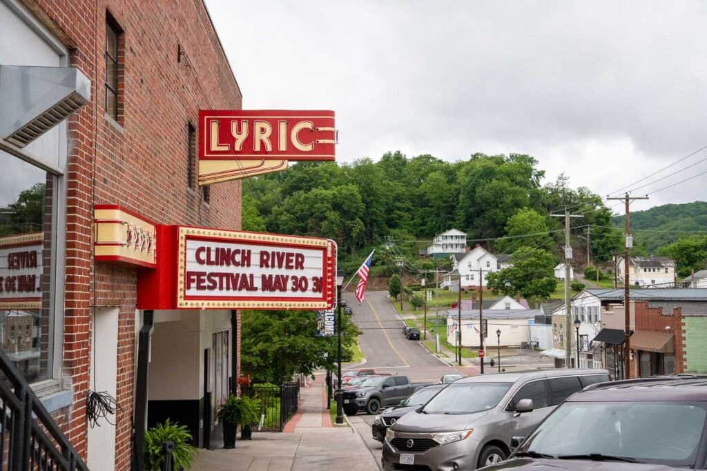 A street view of a small town with a brick theater displaying a marquee for the Clinch River Festival on May 30; cars are parked along the street under a cloudy sky, close to spots featured in western front hotel reviews.