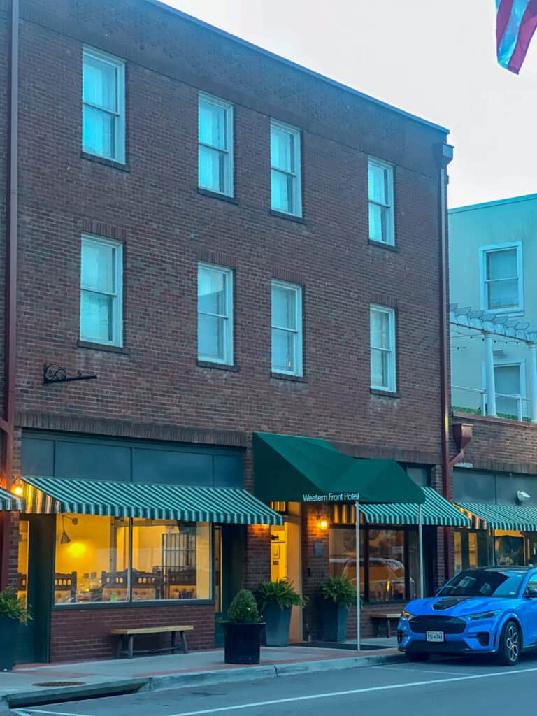 A brick three-story building with green awnings and striped canopies, housing the Western Front Hotel—often praised in Western Front Hotel reviews—with a blue car parked in front on the street.