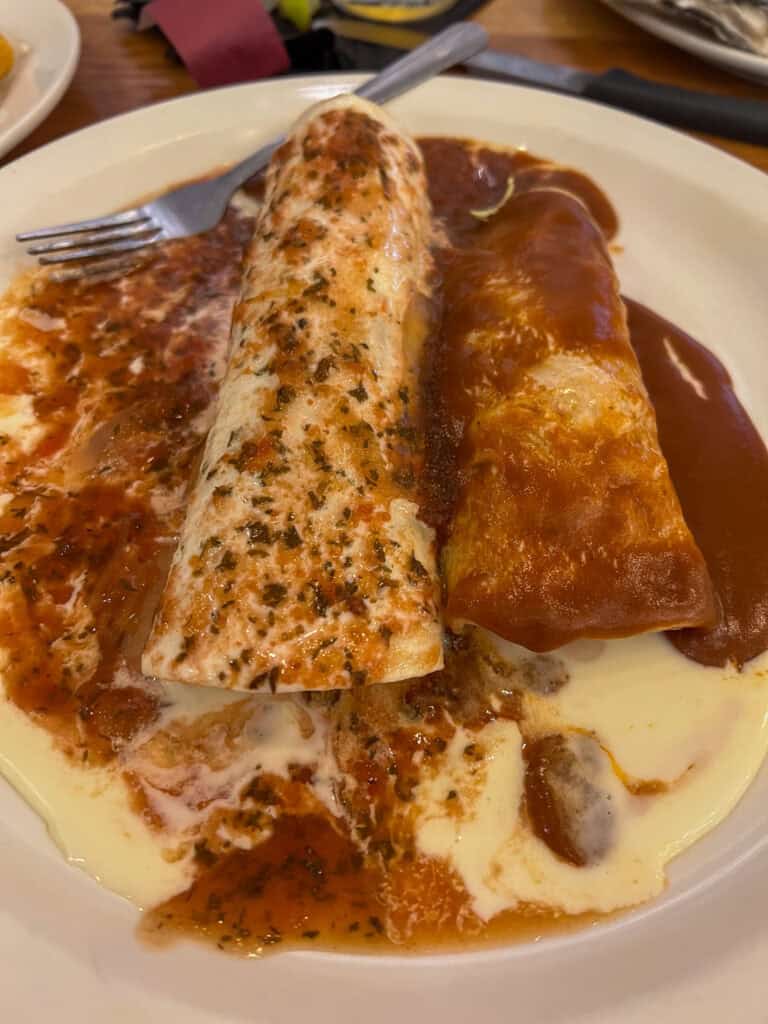 Two enchiladas covered in red sauce and melted cheese, served on a white plate with a fork—just one of the delicious dishes praised in western front hotel reviews.