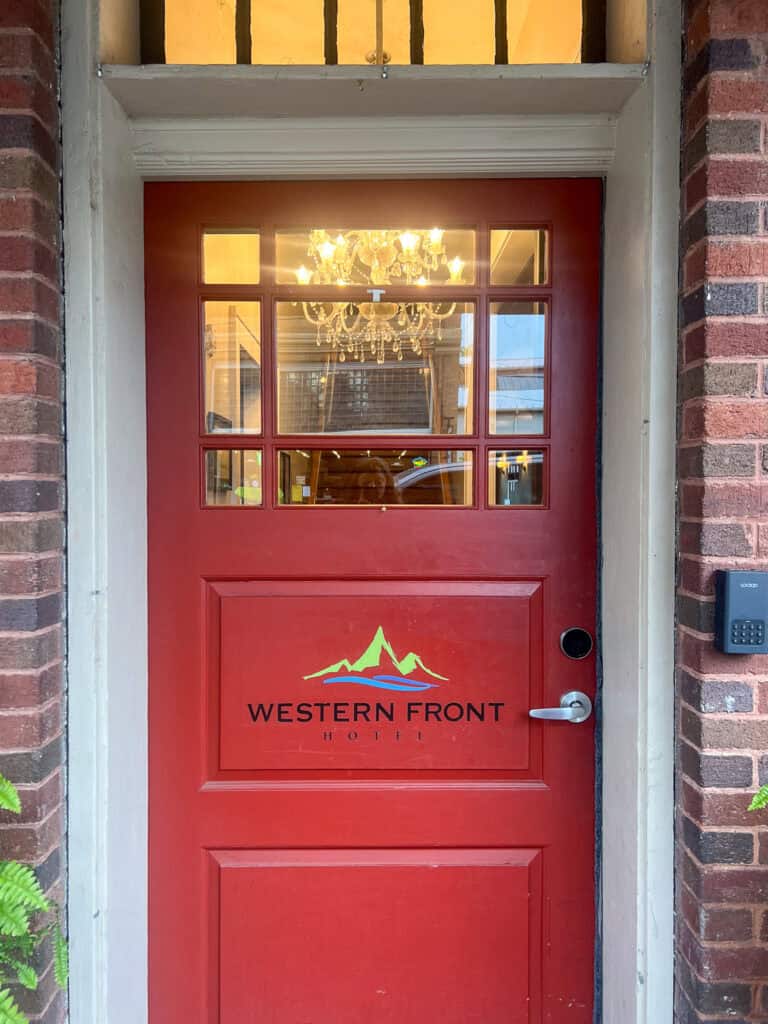 Red door with glass panes and "Western Front Hotel" logo, set in a brick wall, with a keypad to the right and a chandelier visible inside—just like those featured in glowing Western Front Hotel reviews.