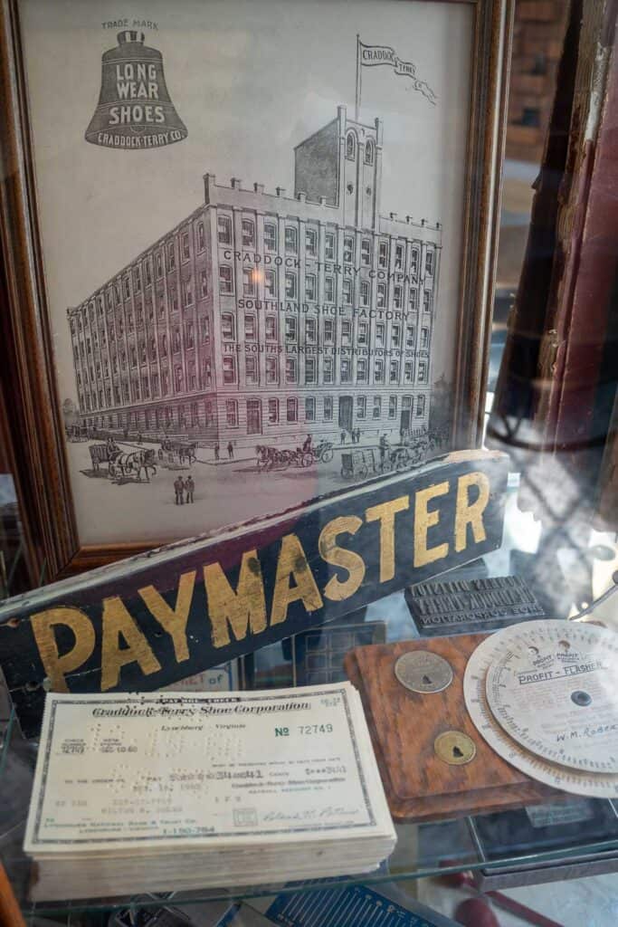 A framed old factory drawing, a "PAYMASTER" sign, vintage checks, and payroll documents are displayed together—a unique touch you might spot at downtown Lynchburg hotels like those mentioned in a Craddock Terry Hotel review.