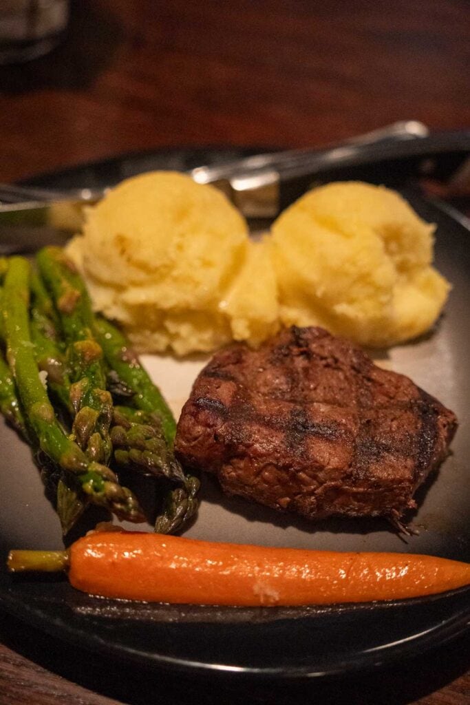 A grilled steak served with two scoops of mashed potatoes, roasted asparagus, and a glazed carrot on a black plate—a dish praised in many Craddock Terry Hotel reviews in downtown Lynchburg hotels.