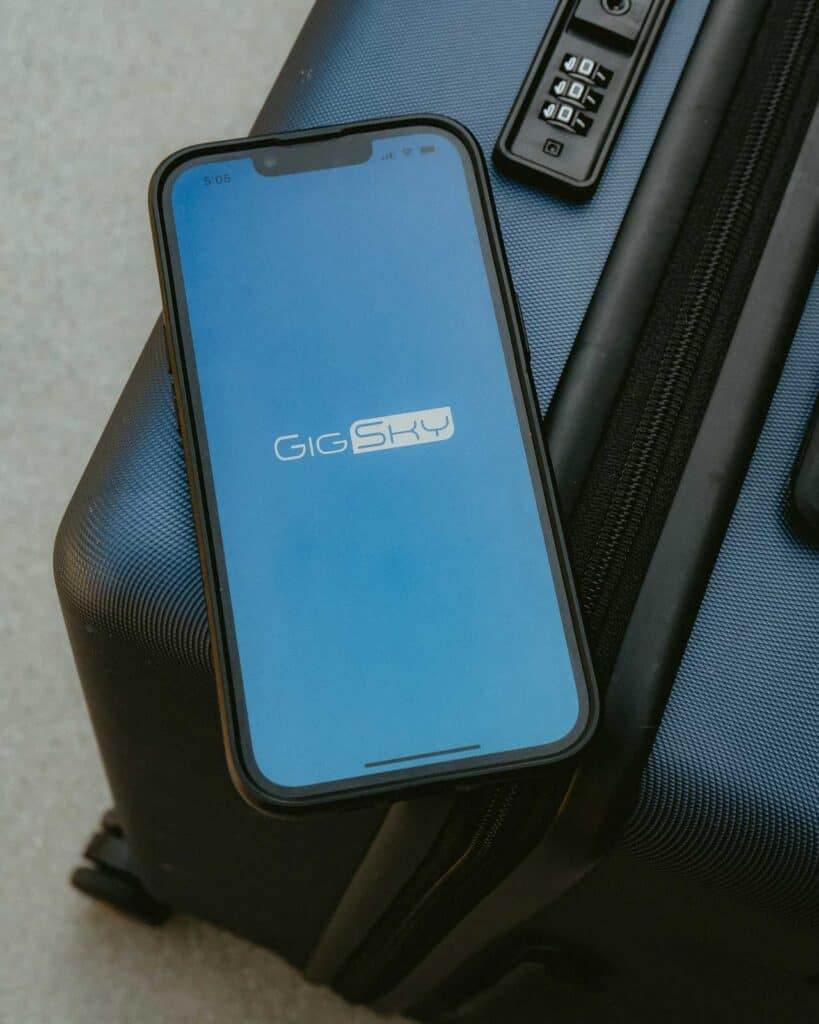 A smartphone displaying the GigSky logo screen rests on top of a dark hard-shell suitcase with a built-in combination lock—perfect for travelers seeking seamless eSIM for Europe connectivity.