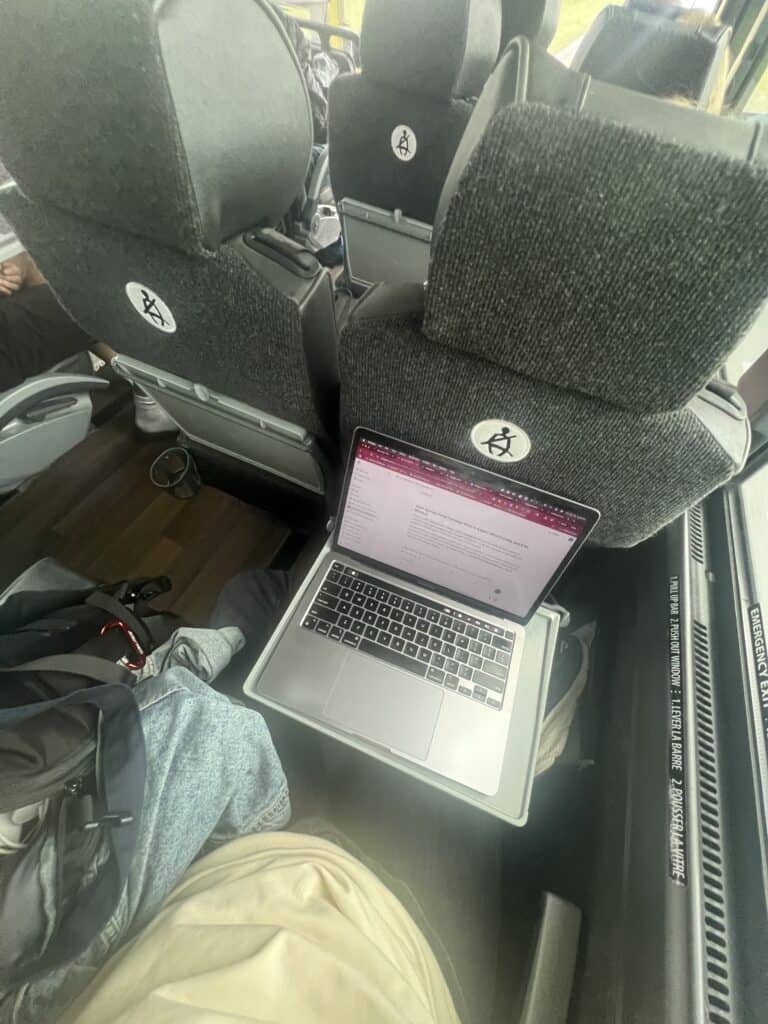 A laptop with an open document rests on a tray table in a bus, perfect for travelers using eSIM for Europe, with seats and a backpack visible nearby.