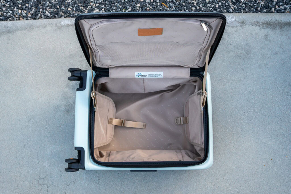 Open, empty suitcase with beige interior, shown from above on a concrete surface next to gravel—perfect for a Level8 luggage review.