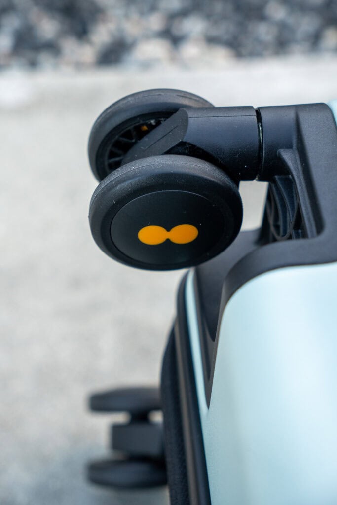 Close-up of a suitcase wheel with a yellow double-dot logo, attached to a light gray suitcase, on a concrete surface—perfect detail for any Level8 luggage review.