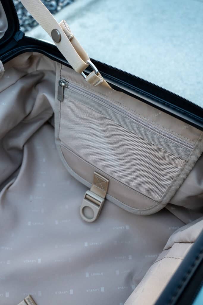 Open suitcase showing beige interior with a zippered mesh pocket, fabric loop, and a metal ring attachment on the lining—features often highlighted in a positive Level8 luggage review.