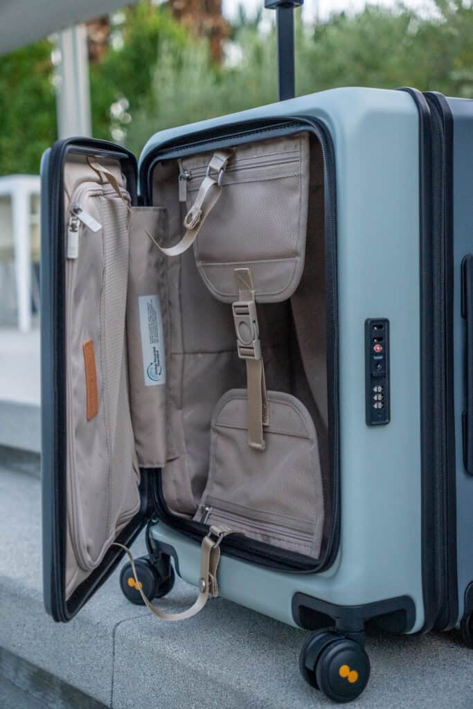 A light blue hard-shell suitcase is open, revealing beige interior compartments, pockets, and straps; it stands on a set of outdoor concrete steps—perfect for a thorough level8 luggage review in real-world settings.