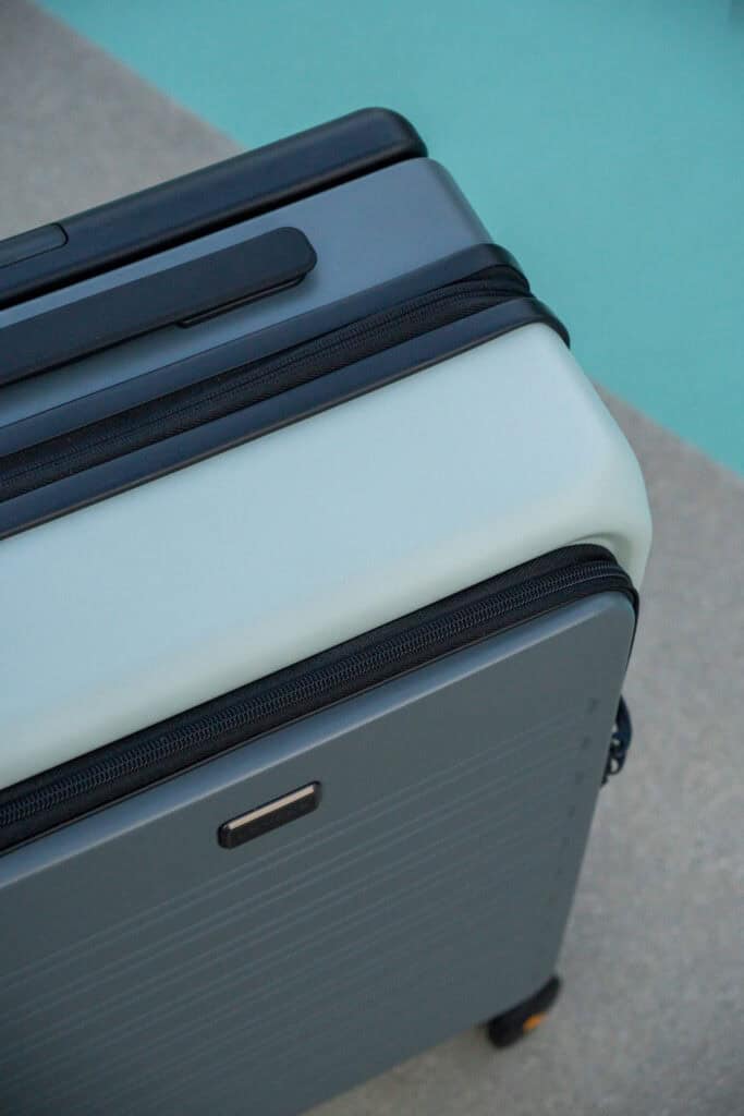 Two hard-shell suitcases, one light gray and one dark gray, are positioned next to each other on a concrete surface beside a pool—ideal for a Level8 luggage review in a stylish travel setting.