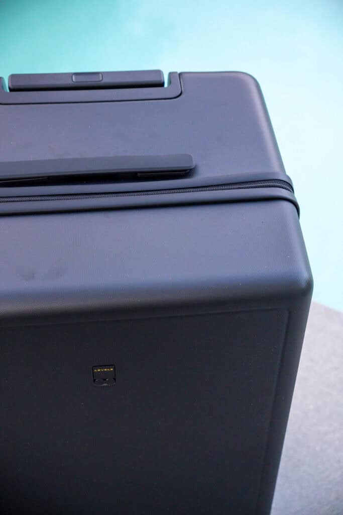 A close-up of a black hard-shell suitcase near a pool, showing the top handle and textured surface—perfect for a detailed LEVEL8 luggage review.