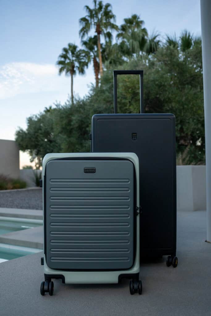 Two hard-shell suitcases, one small and one large, stand side by side on a patio near a pool, with palm trees and modern architecture in the background—a perfect scene for any level8 luggage review.