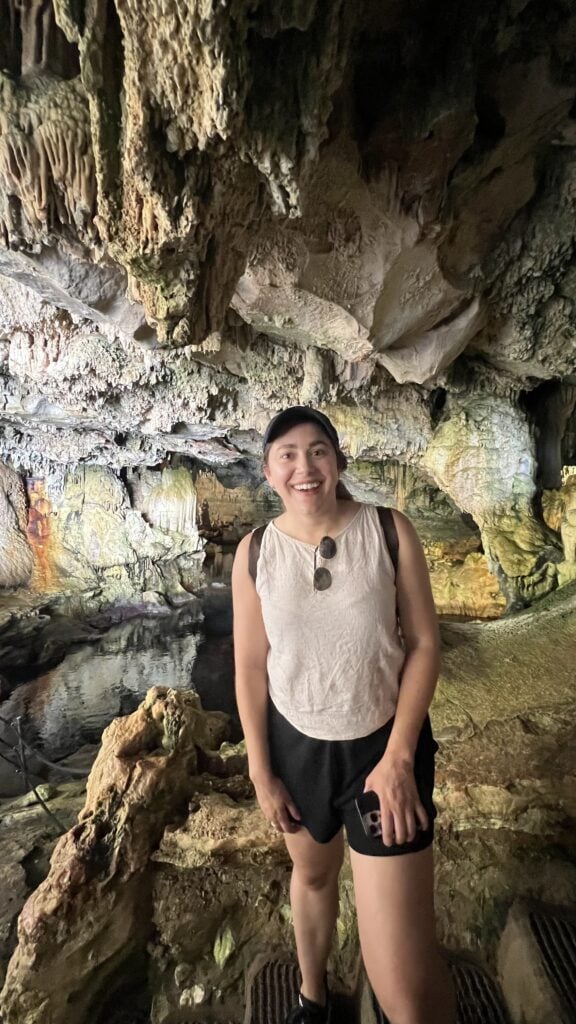 A person standing and smiling inside a cave with rocky, textured walls and formations in the background—one of the unique things to do in Alghero, Sardinia.