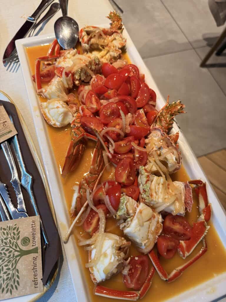 A rectangular plate with crab pieces topped with sliced cherry tomatoes and onions in a reddish sauce, served with cutlery on the side—a delicious taste of Alghero Sardinia to add to your list of things to do in Alghero.