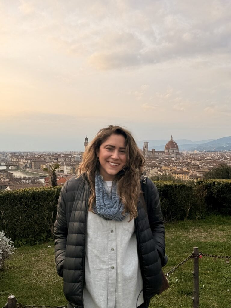 A woman stands outdoors smiling with a cityscape and the Florence Cathedral visible in the background during sunset, perhaps inspired by her language learning plan for exploring Italy.