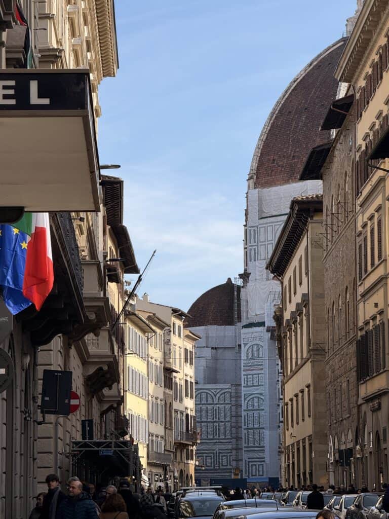 A street in Florence, Italy, with cars parked along the sides, Italian flags hanging, and the Florence Cathedral dome visible in the background—an inspiring setting for creating a language learning plan.