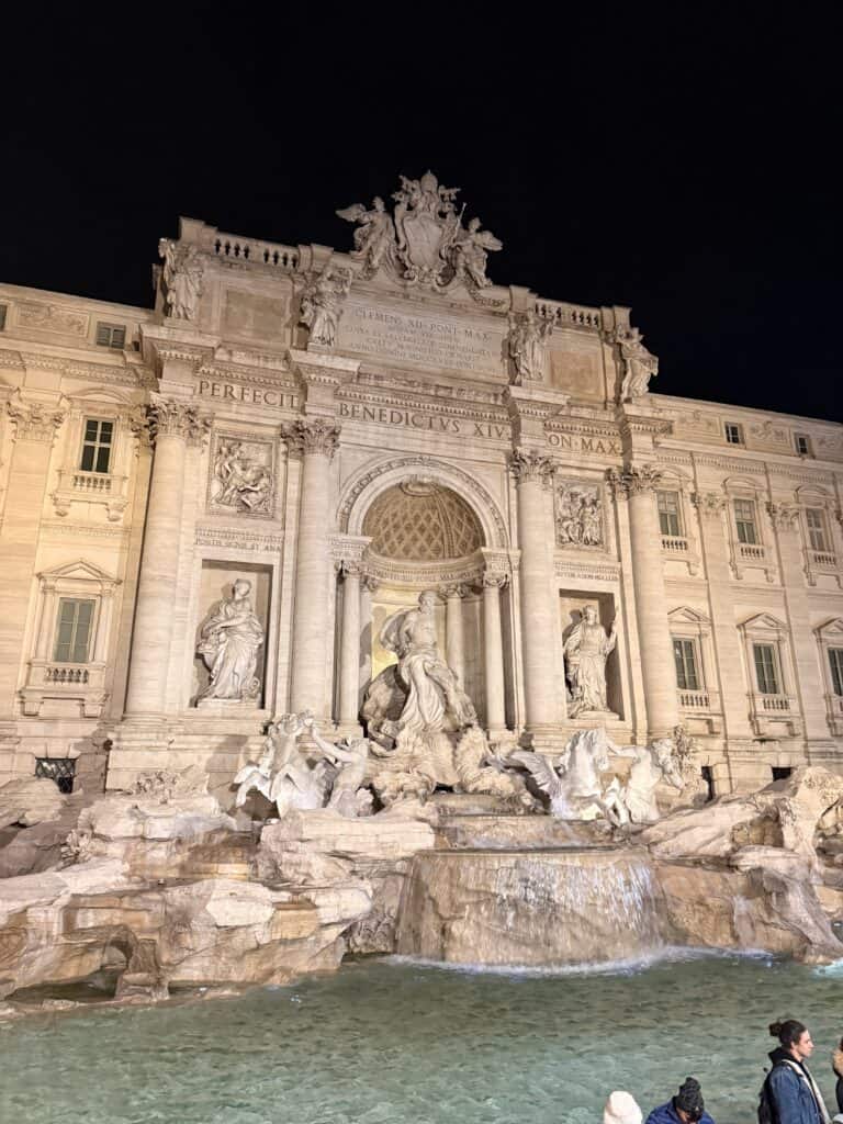 The Trevi Fountain in Rome is illuminated at night, showing detailed sculptures, flowing water, and part of the surrounding historic building—a scene as inspiring as starting a new language learning plan.