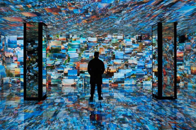 A person stands inside Casa Batlló in a room where the walls, floor, and ceiling are covered in colorful digital images, creating an immersive visual environment.