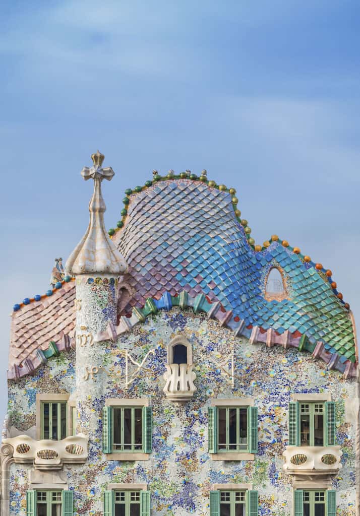 Colorful, ornate building facade with mosaic tiles, arched windows, and an undulating rooftop against a clear blue sky—this stunning exterior captures the imaginative spirit of Casa Batlló.