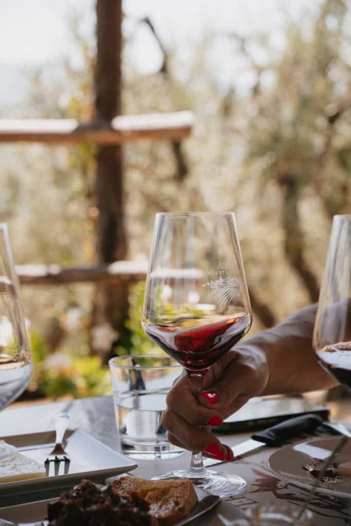 A hand holding a glass of red wine at an outdoor table with food, captured during a 3 days in Florence itinerary.