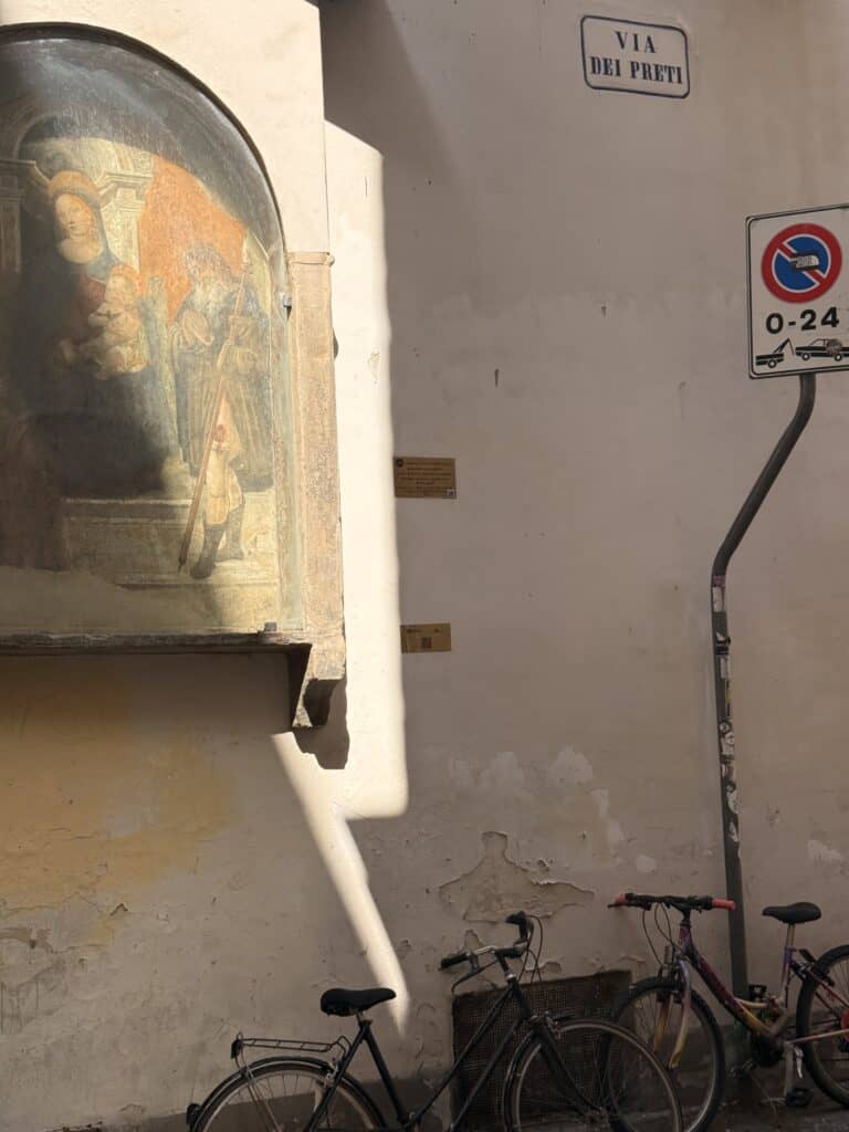 A religious fresco in a wall niche above two parked bicycles on a Via dei Preti street corner, seen during a 3 days in Florence itinerary.