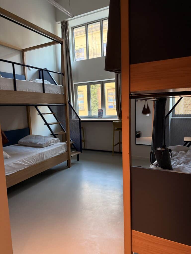 A hostel dorm room for your 3 days in Florence, featuring wooden bunk beds, a central window with bar seating, and privacy curtains.