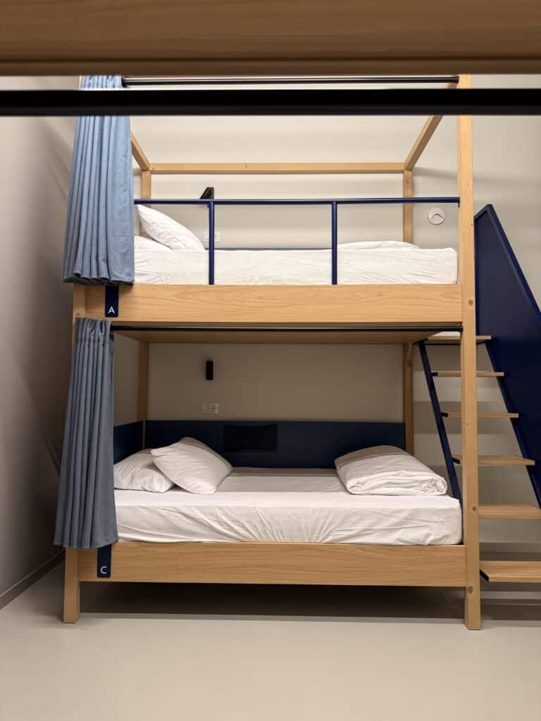 Wooden bunk beds with blue railings, blue curtains, and white bedding labeled A and C, ideal for a 3 days in Florence itinerary.
