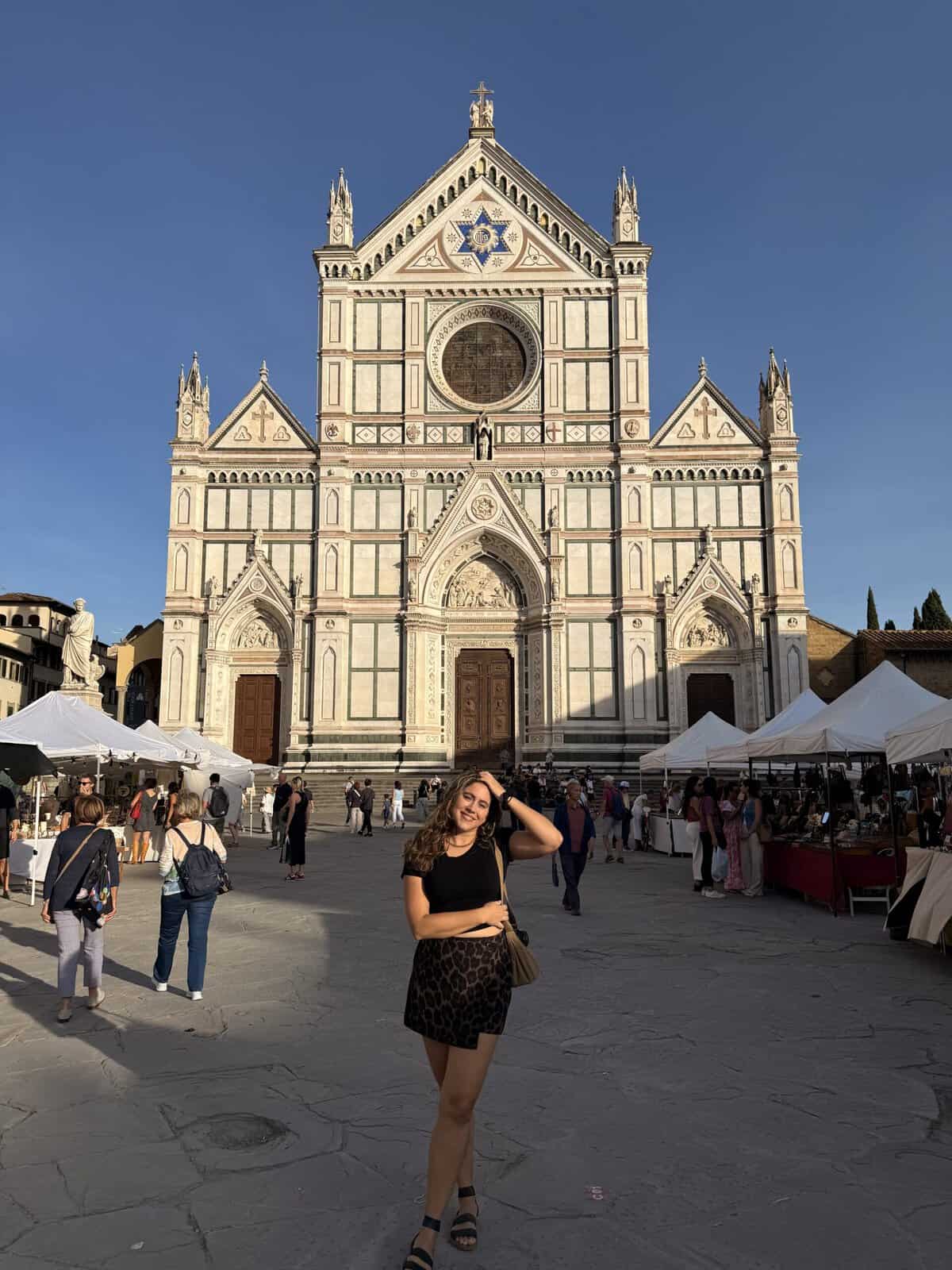 A young woman poses in front of the Basilica of Santa Croce in Florence, surrounded by market stalls during a 3 days in florence itinerary.