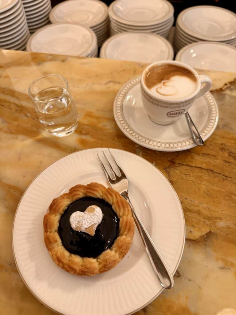 A heart-shaped pastry tart on a plate next to coffee and water, perfect for your 3 days in Florence.