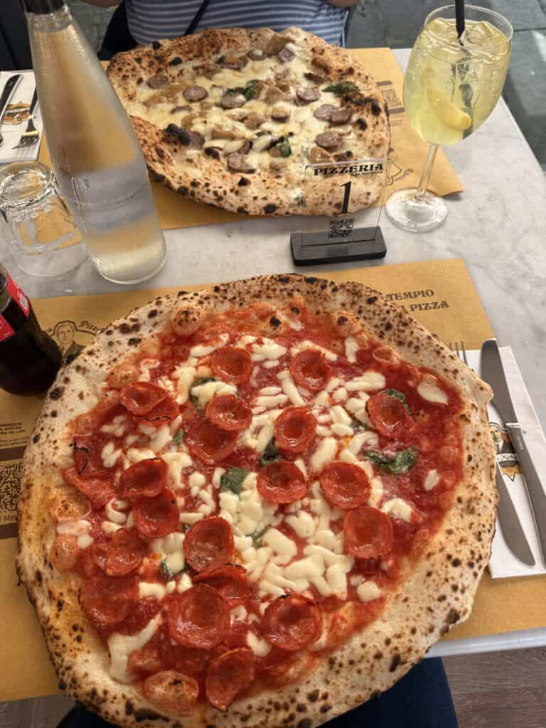 A pepperoni pizza and a sausage and mushroom pizza on a table with drinks and a table number sign, perfect for a 3 days in Florence itinerary.