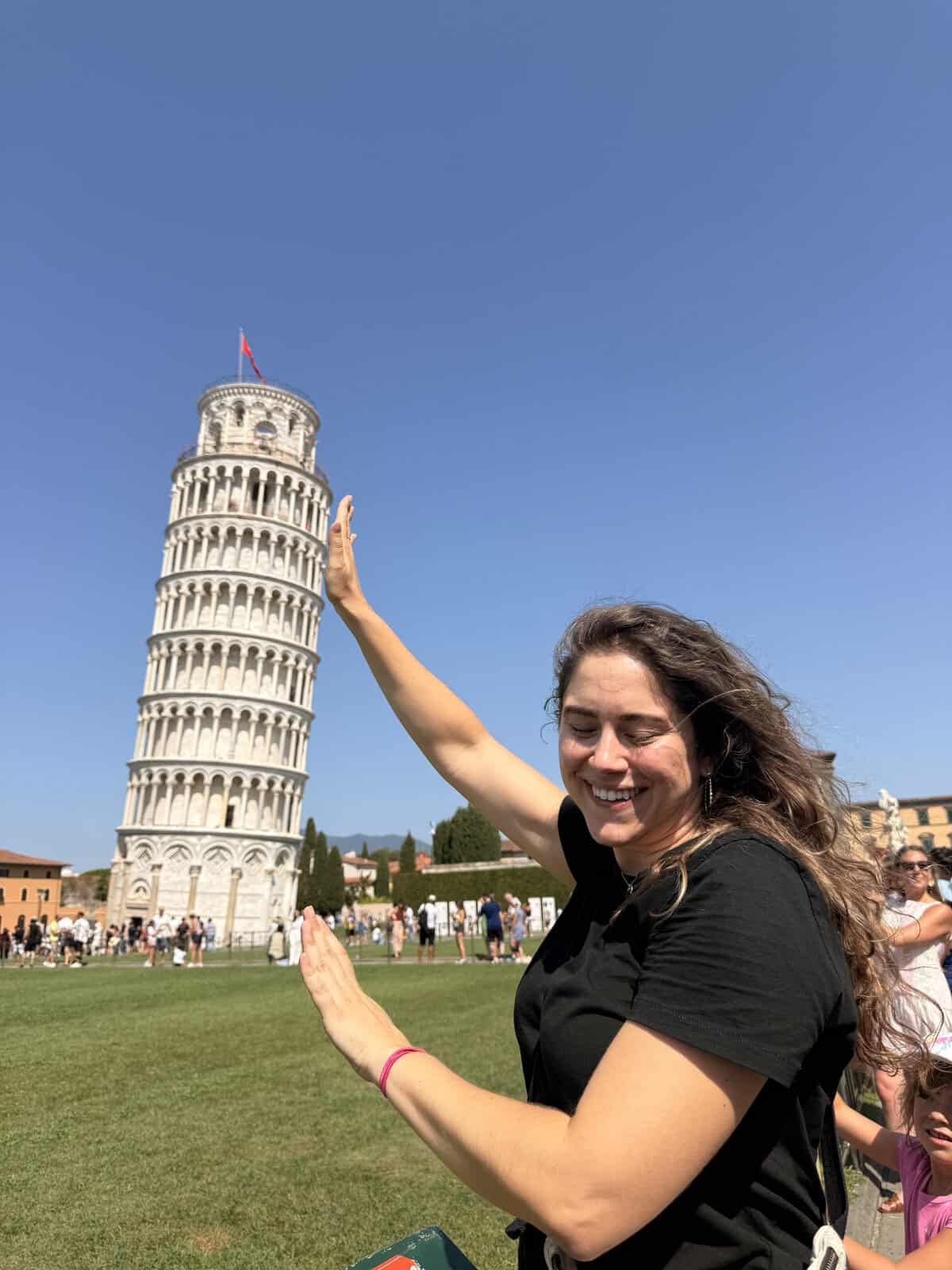 A woman smiling with her arms raised in front of the Leaning Tower of Pisa during a 3 days in Florence itinerary.
